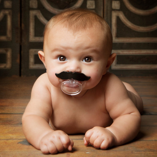 Baby with a mustache pacifier on a wooden floor