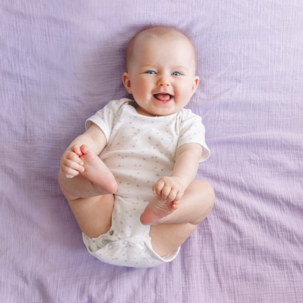 Baby in a white onesie sitting on a purple blanket