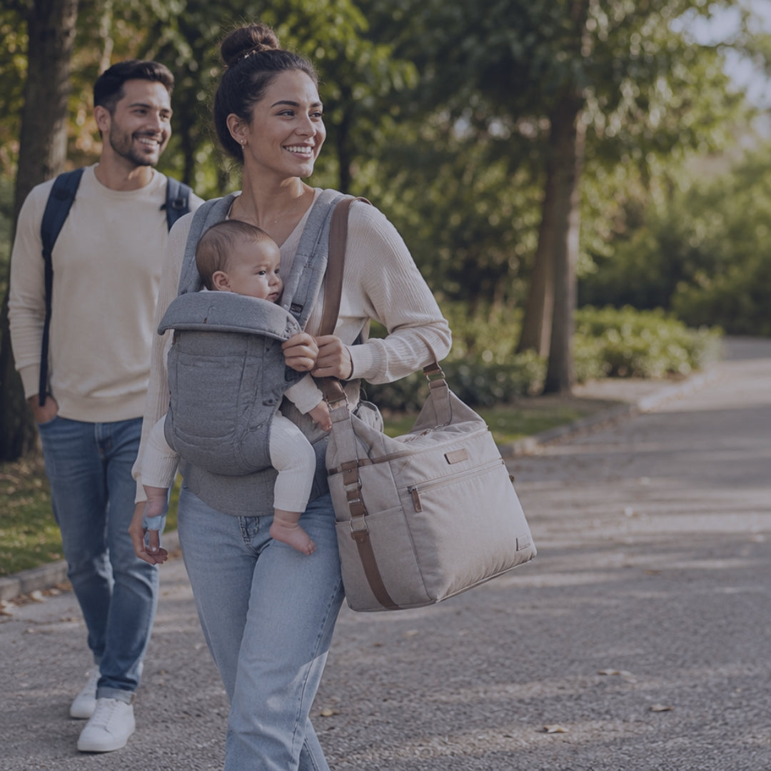 Woman walking with a baby in a carrier and a diaper bag, man walking ahead on a path.