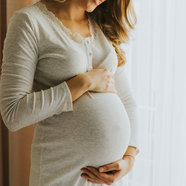 Pregnant woman wearing a light gray outfit, holding her belly.